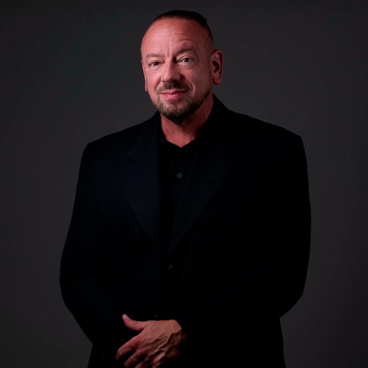 Professional portrait of author David M. Ward wearing a black suit against a dark gray background.